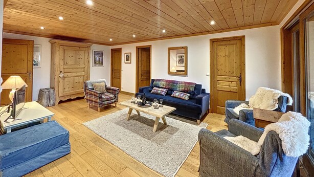 Un salón espacioso con techos de madera, un sofá azul, un sillón de cuadros y una mesita de centro.