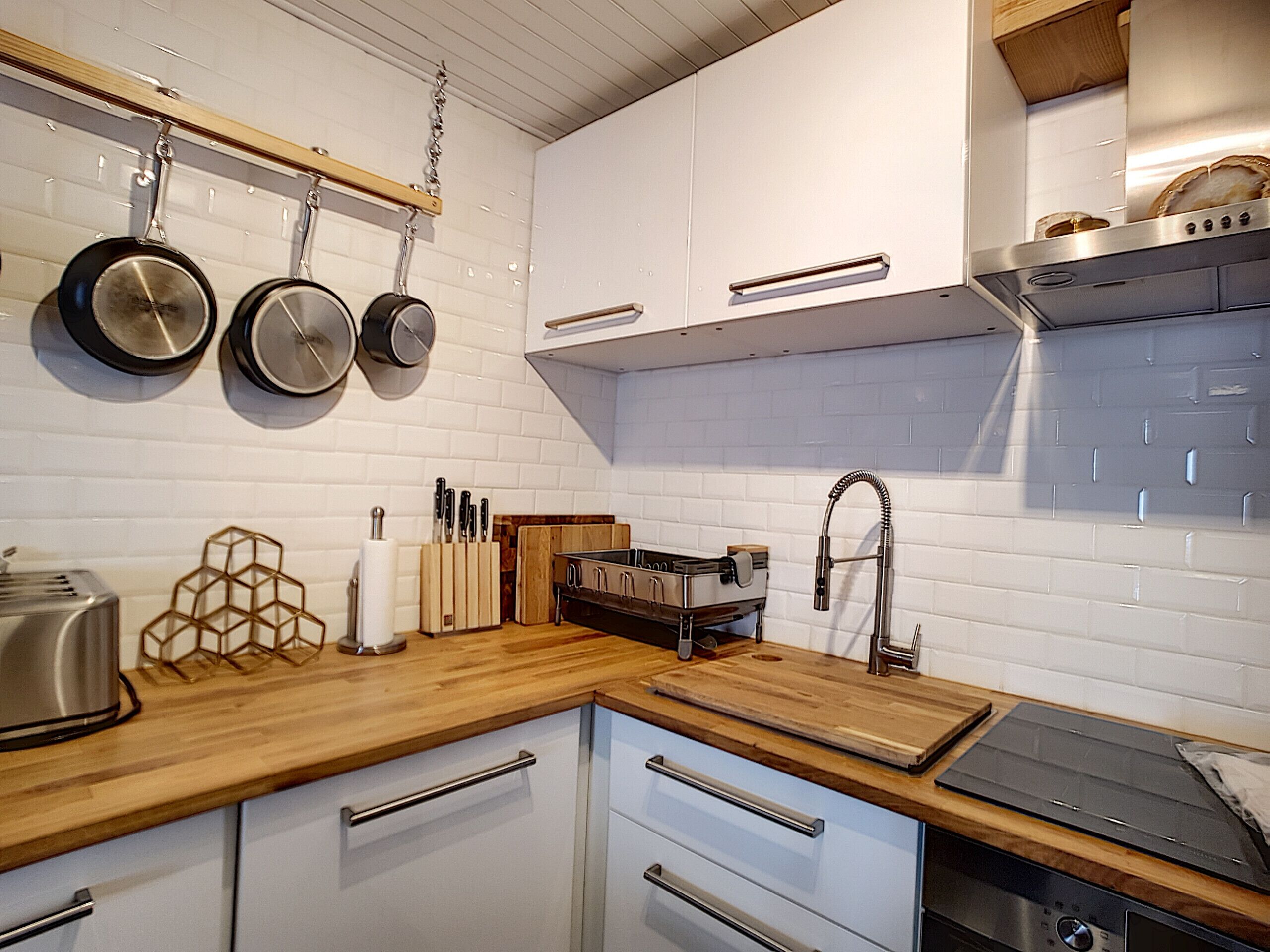A modern kitchen with white cabinets, a wooden countertop, a stainless steel toaster, and hanging pots.