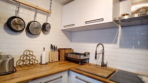 A modern kitchen with white cabinets, a wooden countertop, a stainless steel toaster, and hanging pots. - Montana - appartement - 6pers - proche centre (Les Gets)