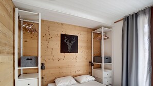 A bedroom with a bed, a wardrobe, a shelf with storage boxes, a wall-mounted deer head artwork, and a window with curtains. - Montana - appartement - 6pers - proche centre (Les Gets)
