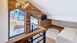 A modern loft bedroom with a large skylight, wooden beams, a chandelier, and a view of a village.