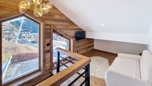 A modern loft bedroom with a large skylight, wooden beams, a white sofa, and a chandelier.