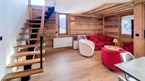 A wooden interior with a staircase, red sofa, and a table.