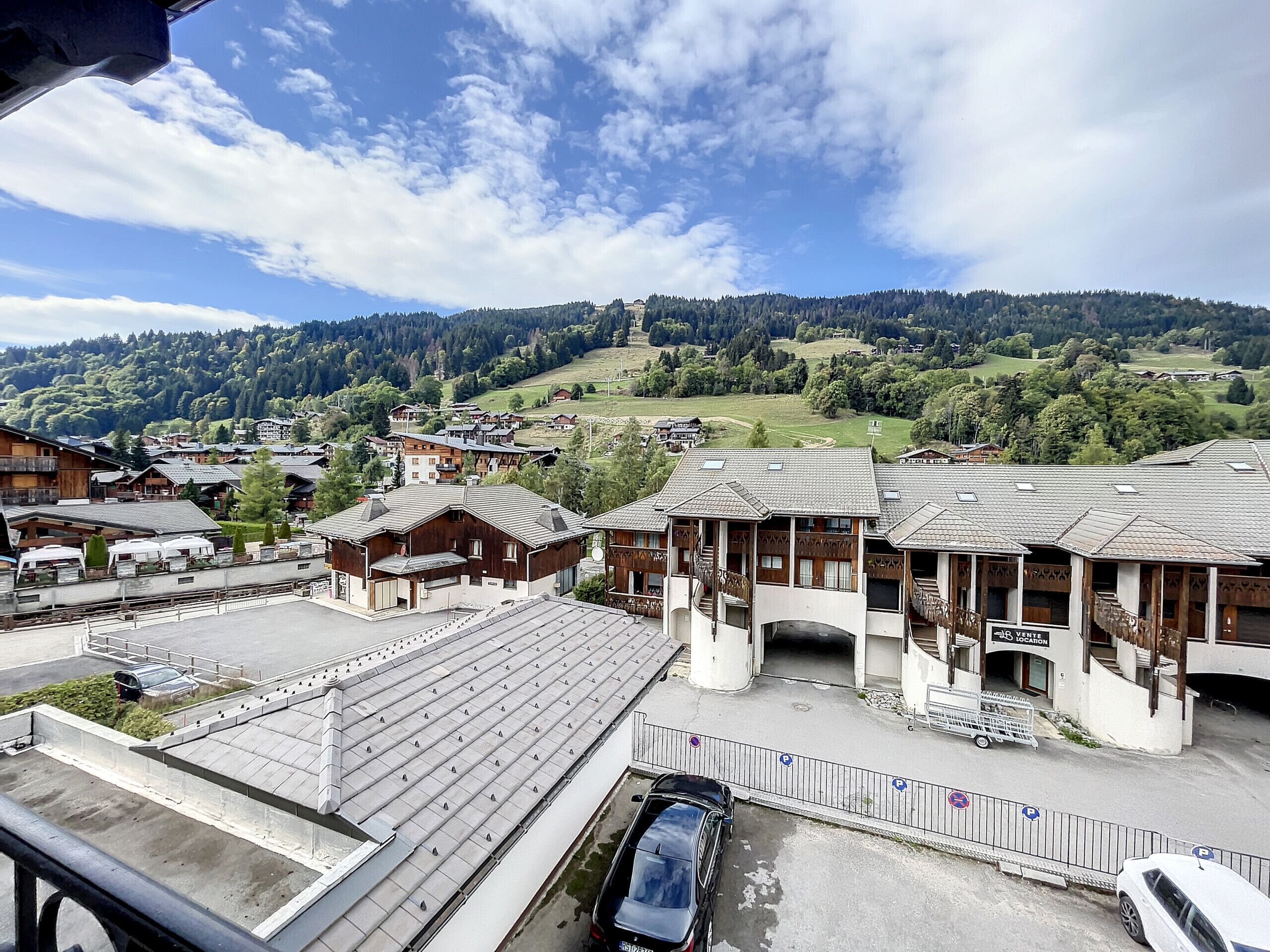 A hotel with a traditional wooden facade, a parking area, and a view of a mountainous landscape.