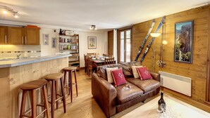 A cozy interior with a kitchen, dining area, and living room featuring wooden walls, a leather sofa, and a mountain landscape painting.