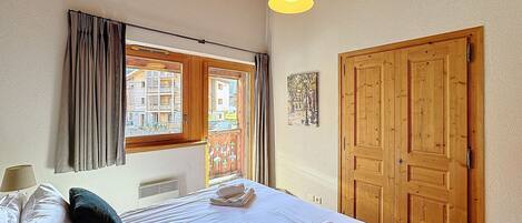 A bedroom with a bed, curtains, a wooden door, and a window with a view of buildings.