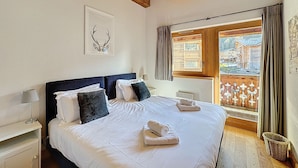 Ein Schlafzimmer mit einem großen Bett, Holzboden, einem Fenster mit Vorhängen und einem gerahmten Bild an der Wand.