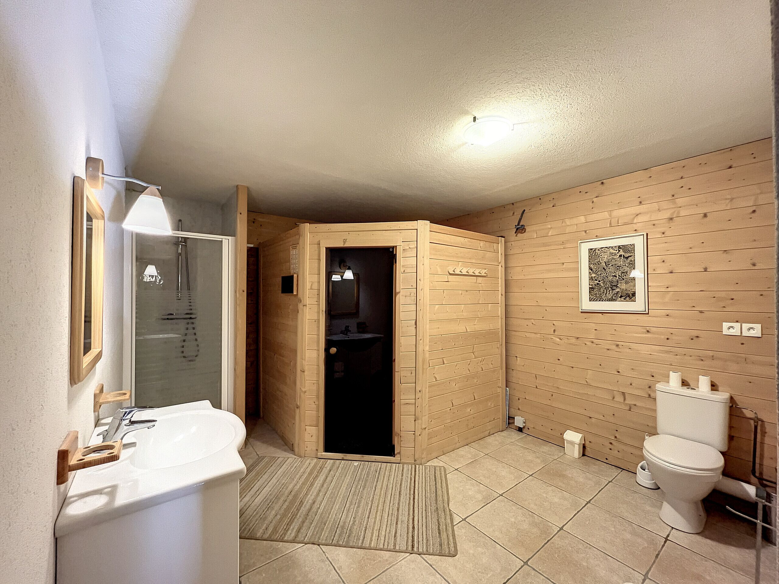 A modern bathroom with a wooden wall, a white sink, a toilet, and a shower area.