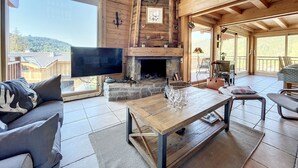 Ein großzügiger Wohnbereich mit Kamin, Holzmöbeln und einem großen Fenster mit Blick auf die umliegende Landschaft.