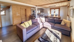 Ein modernes Wohnzimmer mit einer Eckcouch, Holzboden und einem Essbereich mit Tisch und Stühlen.