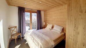 Ein Schlafzimmer mit Holzwänden, einem Bett, Vorhängen, einem Stuhl und einem Fenster.