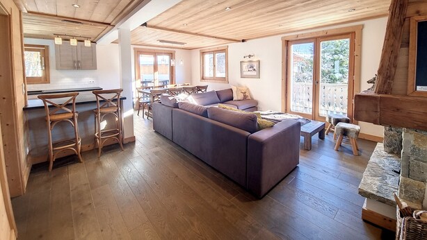 Ein Holzinnenraum mit einer Couch, einem Esstisch, Stühlen und einem Steinkamin.