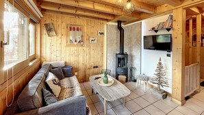 A cozy wooden cabin interior with a sofa, a table, a fireplace, and a television. - Chalet Noisette -8 pers - proche centre (Les Gets)