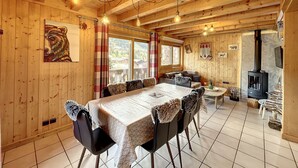 A wooden cabin interior with a dining table, chairs, a sofa, a fireplace, and a bear painting on the wall. - Chalet Noisette -8 pers - proche centre (Les Gets)