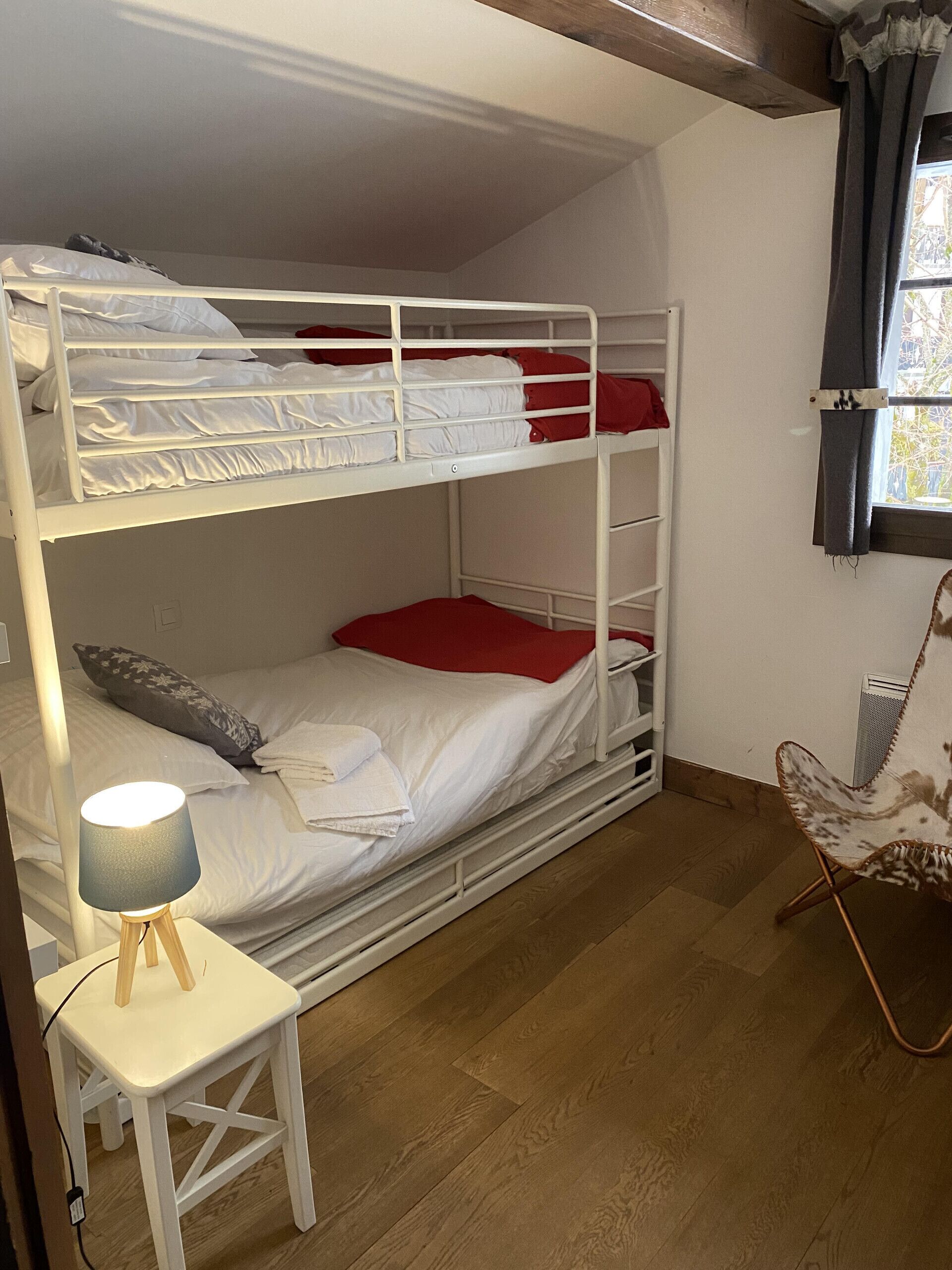 Een slaapkamer met stapelbed, een klein tafeltje en stoel, een lamp en een raam met gordijnen.