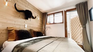 A bedroom with a wooden headboard, a bed with multiple pillows, a wall-mounted light fixture, and a window with curtains. - Les 3 Sapins - appartement4pers - centre station (Les Gets)