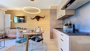 A modern kitchen with a wooden wall, a bull skull decoration, a round light fixture, and a dining area with clear chairs and a marble table. - Les 3 Sapins - appartement4pers - centre station (Les Gets)