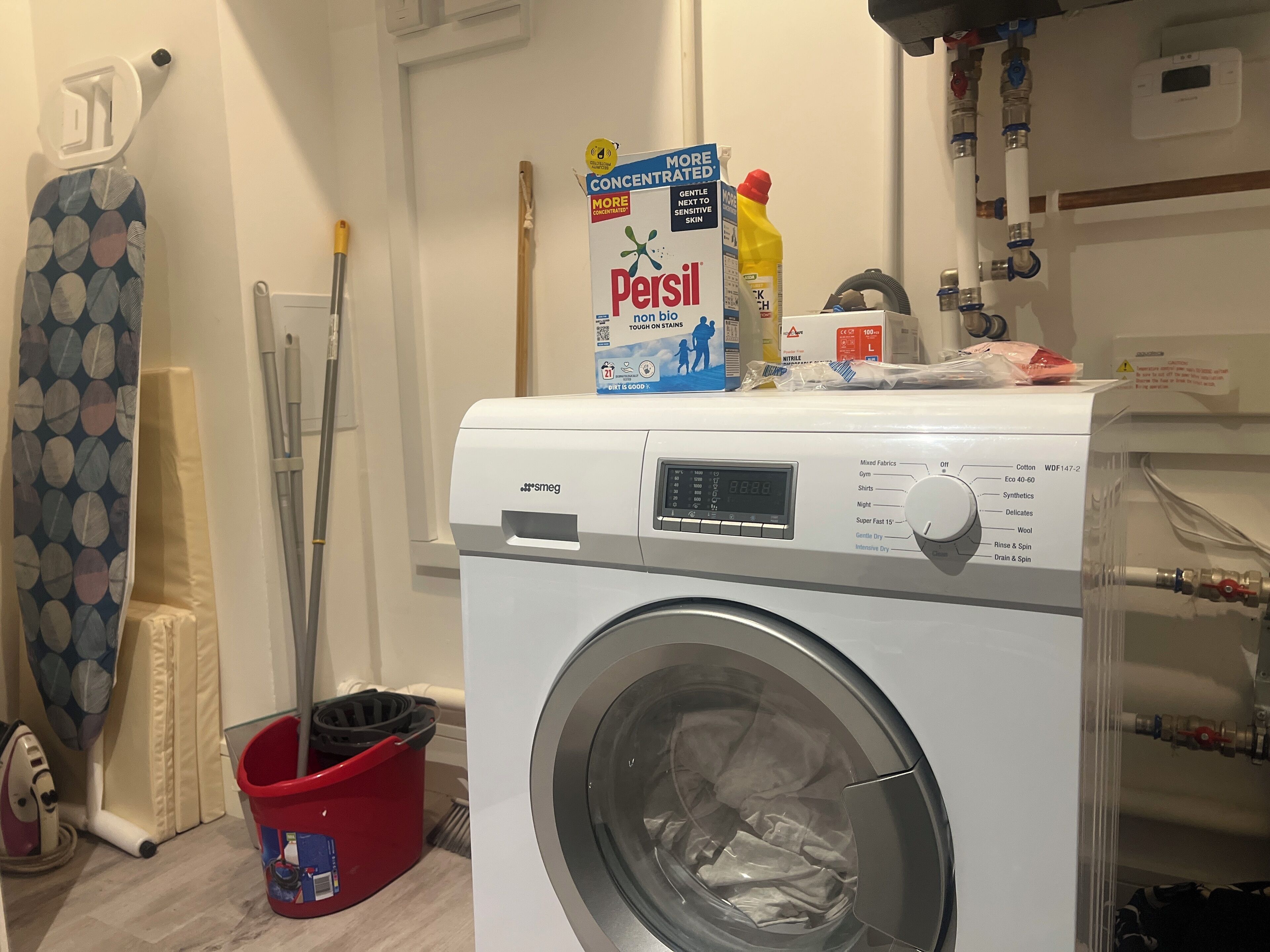 A front-loading washing machine with a control panel, a red bucket, and a blue Persil detergent box.
