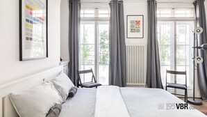 Et moderne soveværelse med en stor seng, to stole, en radiator og et vindue med gardiner.