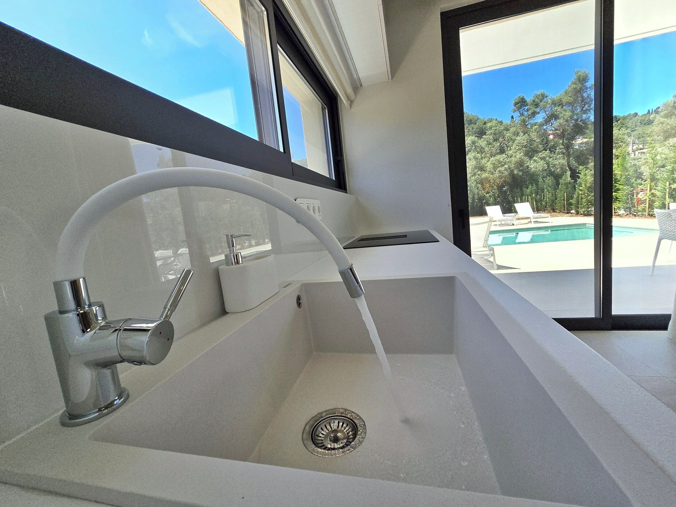 A modern bathroom with a white sink, chrome faucet, and a window overlooking a pool area.