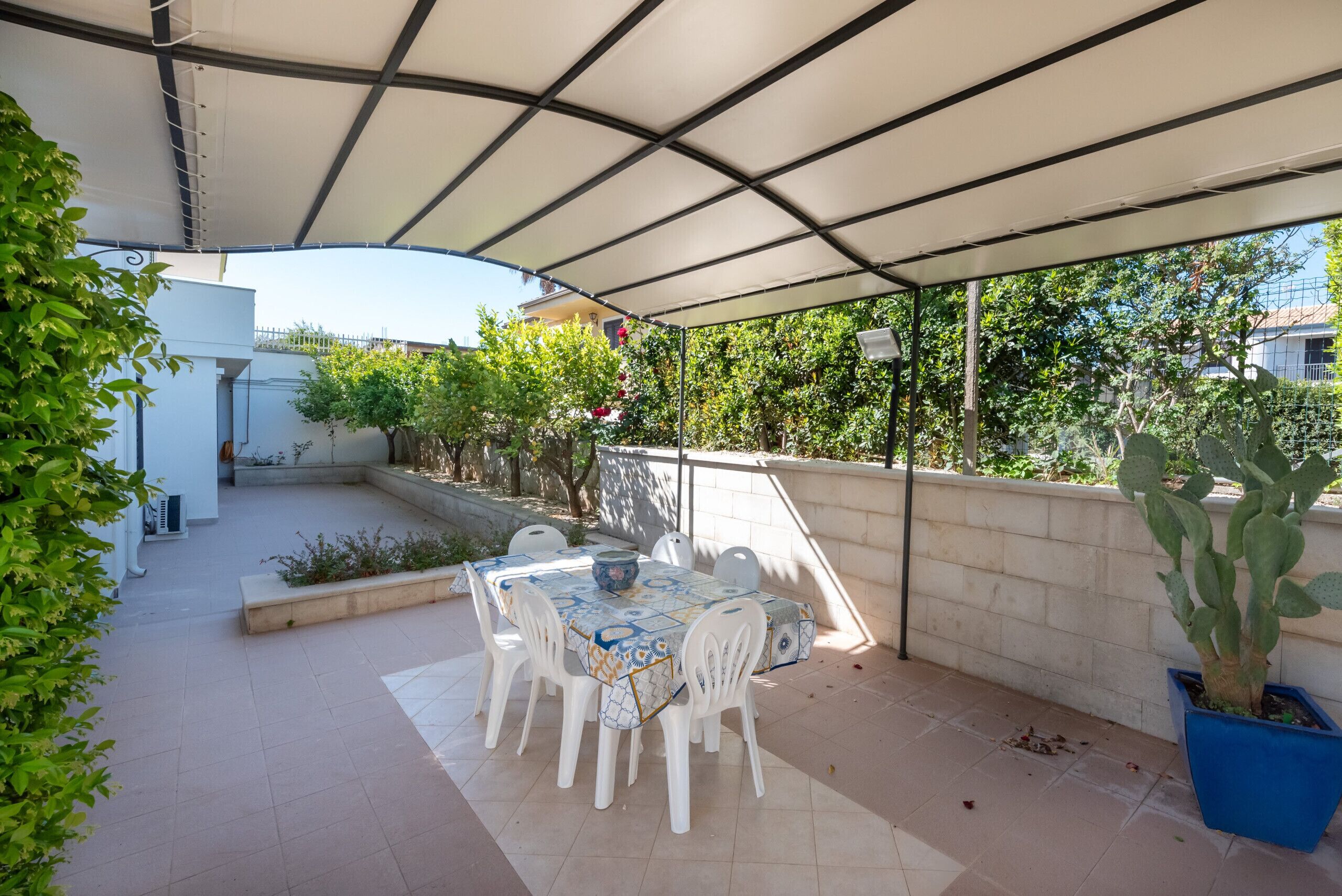 Eine Terrassesituation mit Tisch und Stühlen, einem überdachten Bereich und Kübelpflanzen.