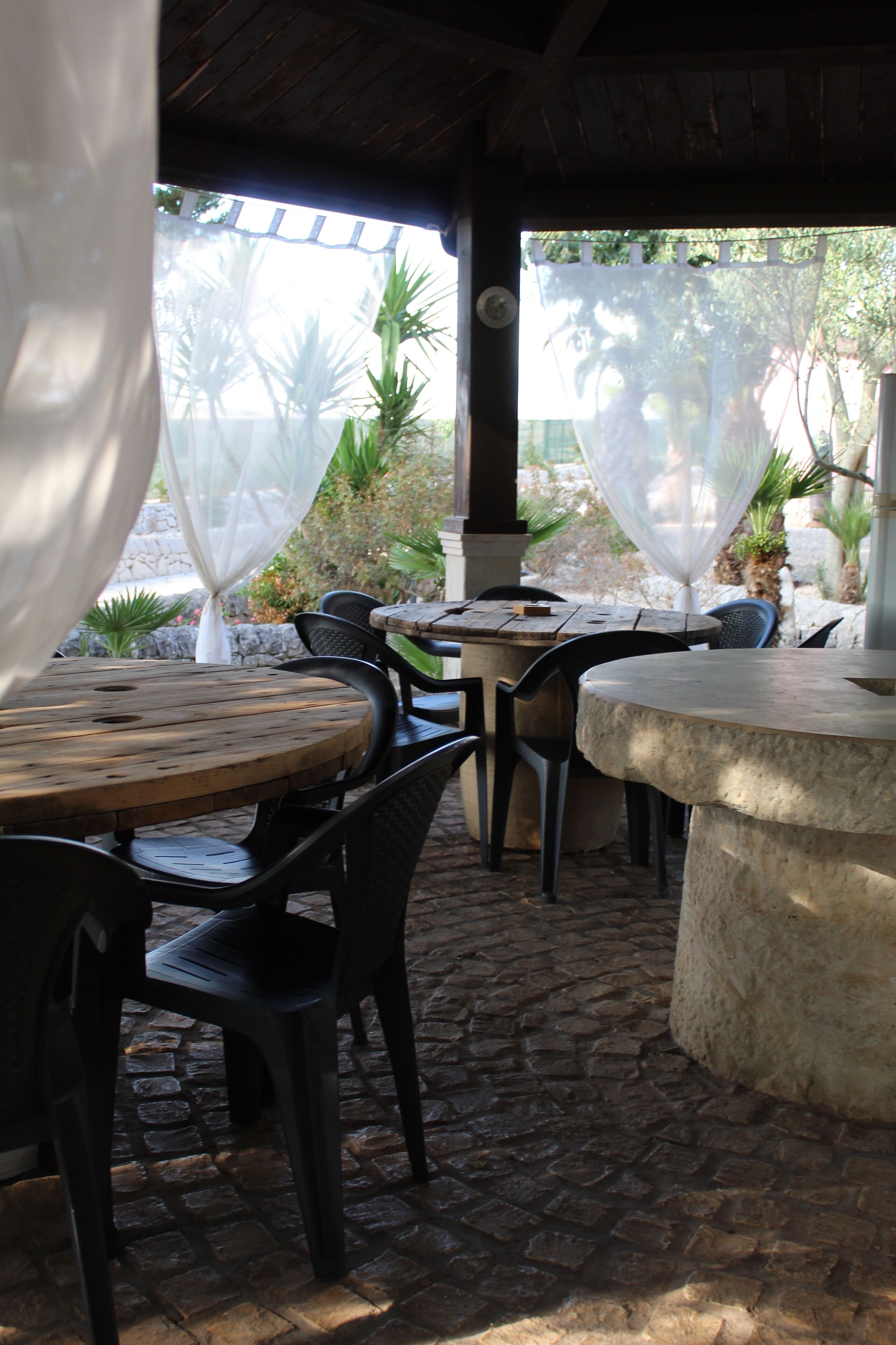 An outdoor patio with stone flooring, wooden tables, and black plastic chairs.