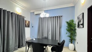 Een vergaderruimte met een tafel, stoelen, grijze gordijnen, een airconditioning en een kamerplant.