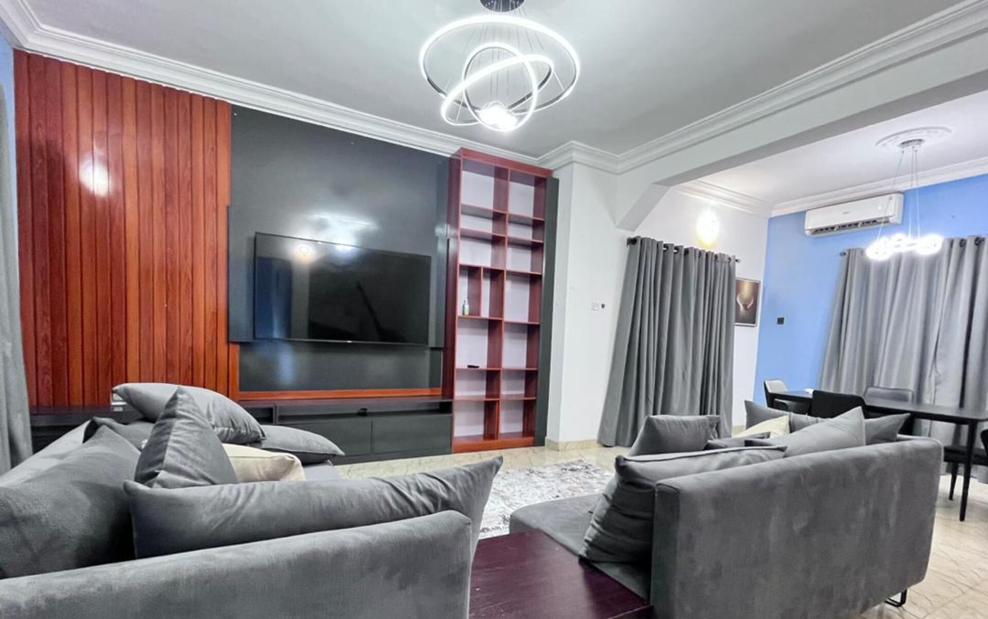 Una sala de estar moderna con un televisor de pantalla plana, sofás grises, una pared de acento de madera y una estantería empotrada.
