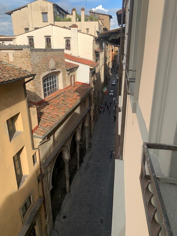 A narrow street with buildings on either side, featuring arched windows and a tiled roof.
