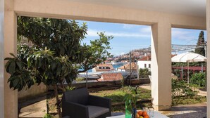 A balcony with wicker furniture, a table with fruit, and a view of a coastal town.