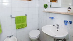 A bathroom with white tiles, a green towel, a bidet, a sink, a mirror, and a small plant.