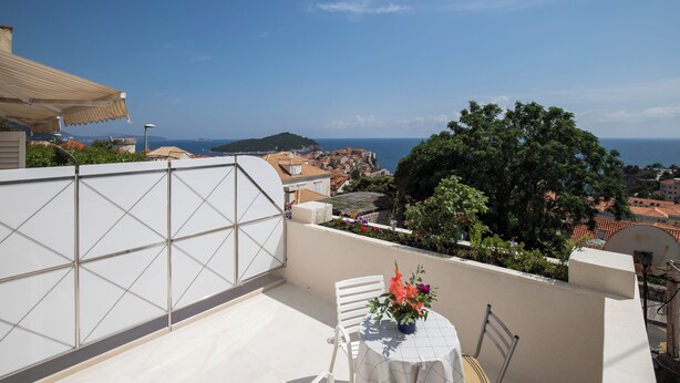A balcony with a table and chairs, overlooking a coastal town with buildings and a view of the sea. - Apartment Bim (Dubrovnik)