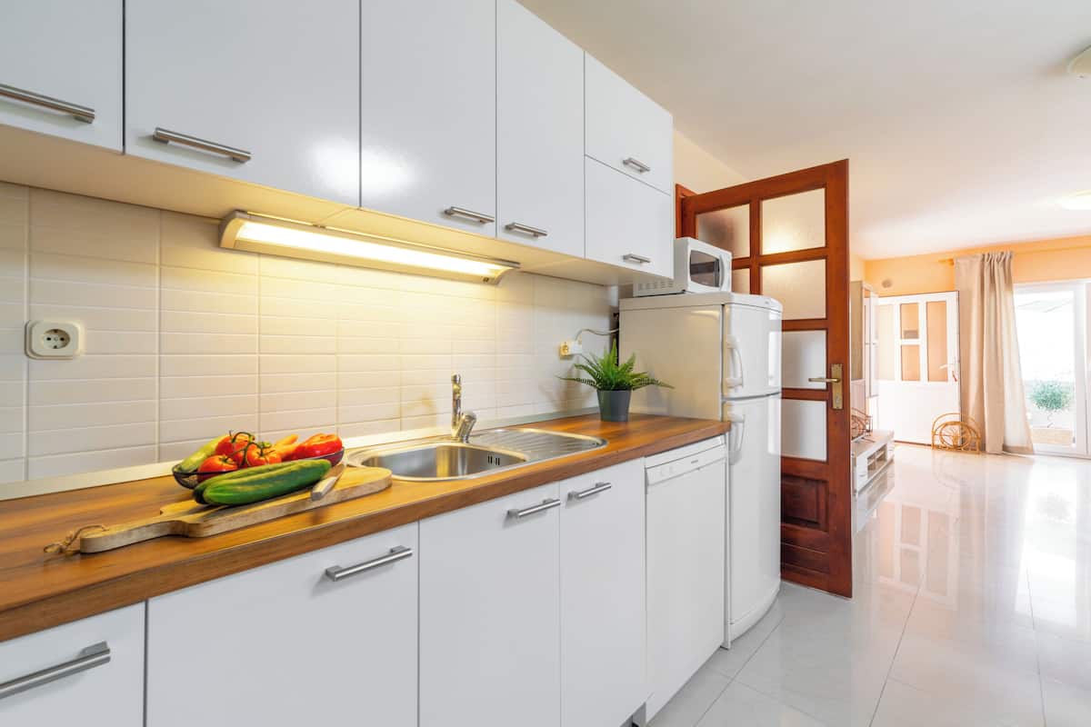 Une cuisine moderne avec des meubles blancs, un plan de travail en bois, un évier et un four à micro-ondes.