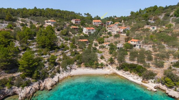 Vue aérienne d’un village côtier, avec des maisons construites sur une colline surplombant une mer turquoise aux eaux limpides.