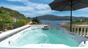 Un bain à remous avec vue sur un lac et des montagnes, un parasol et une rambarde.