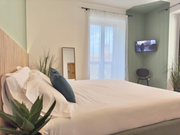 A modern bedroom with a bed, a TV, a chair, and a potted plant.