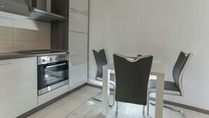 Una cocina moderna con horno empotrado, campana extractora de acero inoxidable y comedor con mesa blanca y sillas negras.