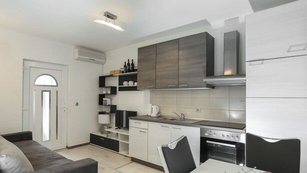 Una cocina moderna con armarios blancos, horno integrado y comedor con mesa y sillas.