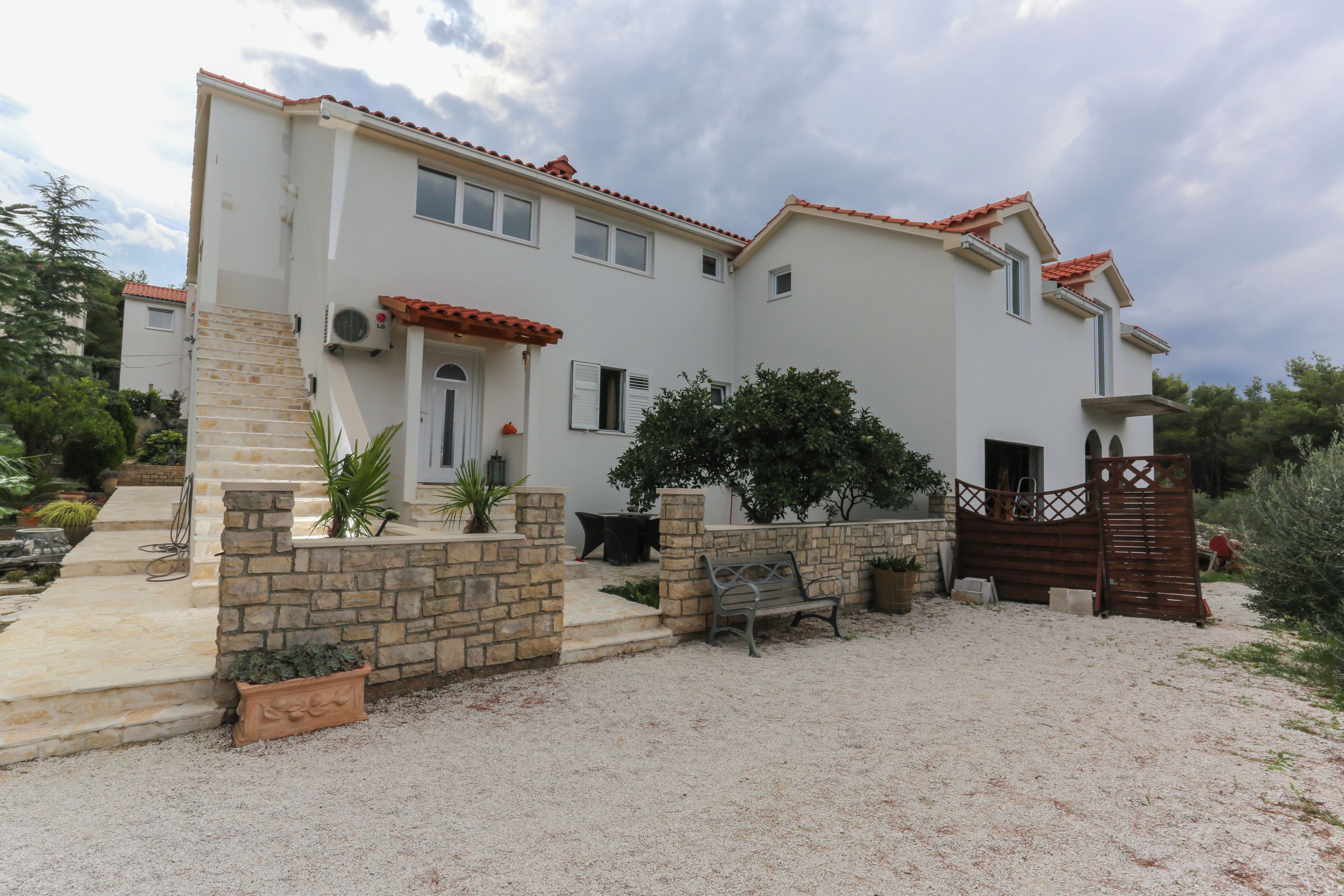 A two-story house with a stone staircase, a wooden bench, and a gravel driveway.