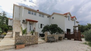 Una casa de dos pisos con una escalera de piedra, un banco de madera y un camino de entrada de grava.