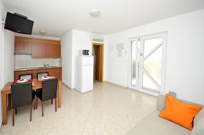 A compact living space with a kitchenette, dining area, and a sofa with an orange cushion. - Apartments Villa Moonlight (Okrug)
