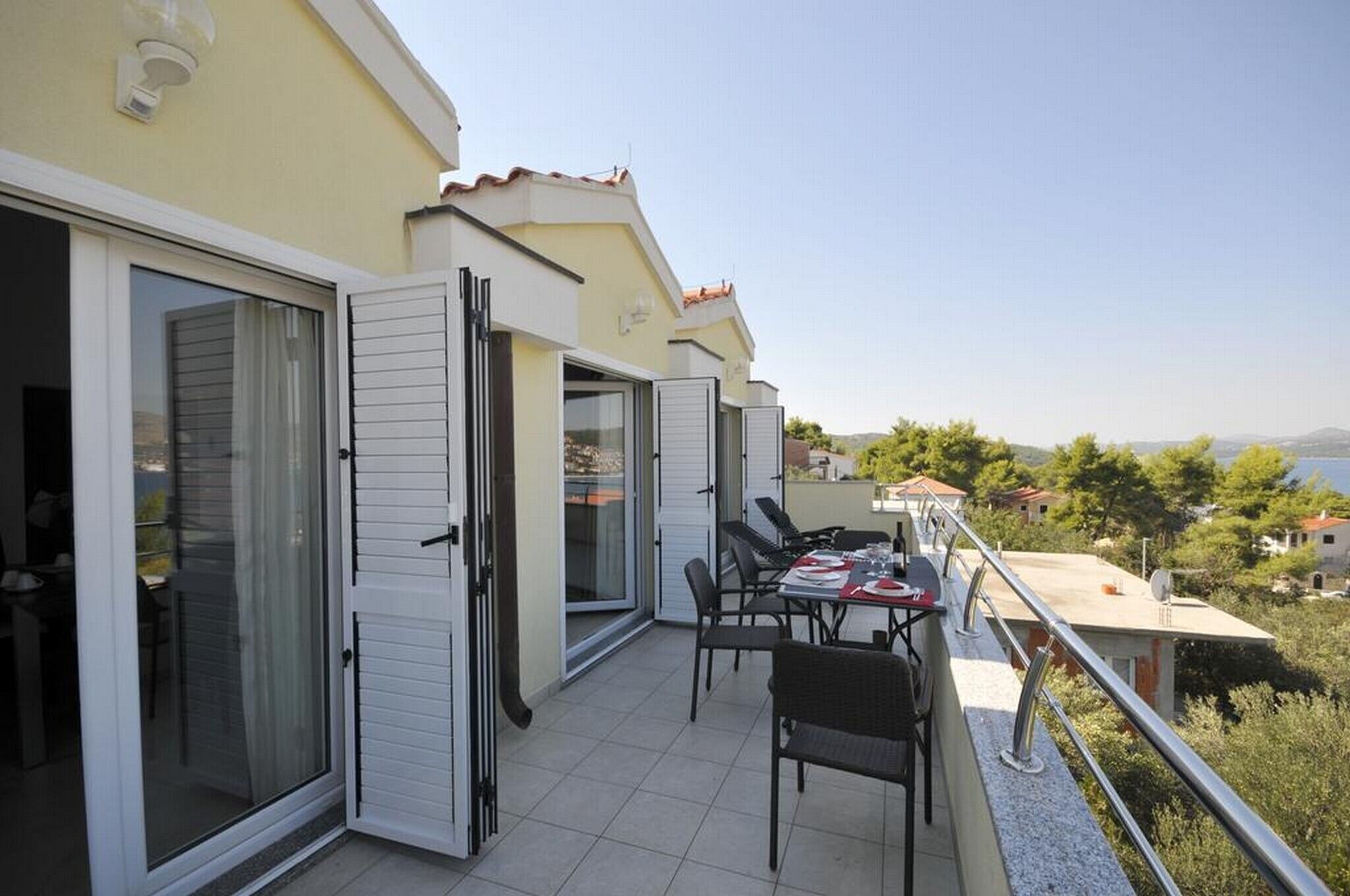 A balcony with a table and chairs, a sliding glass door, and a view of the sea and hills.