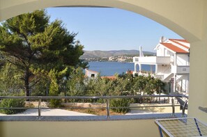 A coastal view with a tree, a white building with a red roof, and a clear blue sea. - Apartments Villa Moonlight (Okrug)