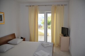 A hotel room with a bed, a television on a stand, and a sliding glass door leading to an outdoor area. - Apartments Villa Moonlight (Okrug)