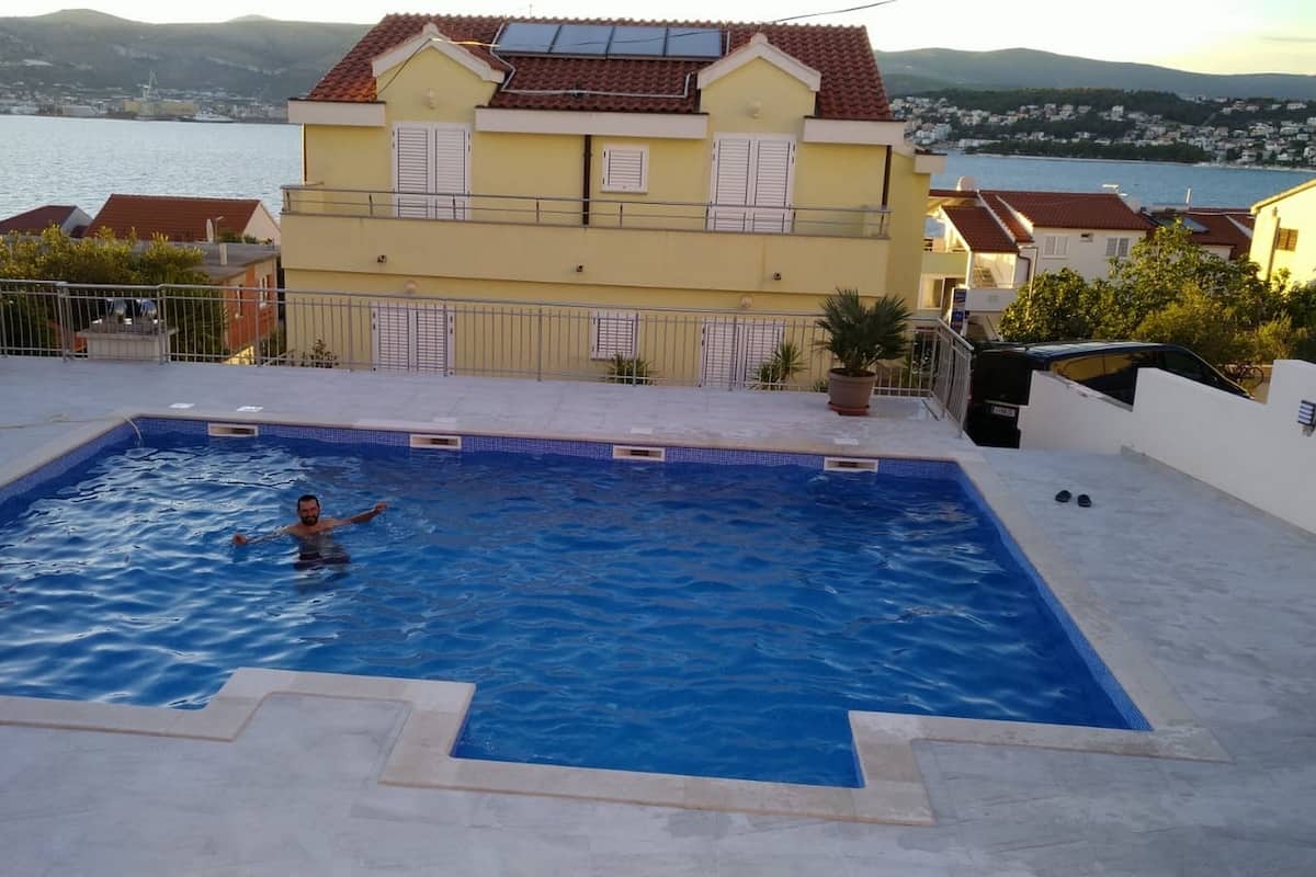 Une piscine avec une personne dans l’eau, entourée d’un balcon d’où l’on peut admirer une étendue d’eau et des bâtiments en arrière-plan.