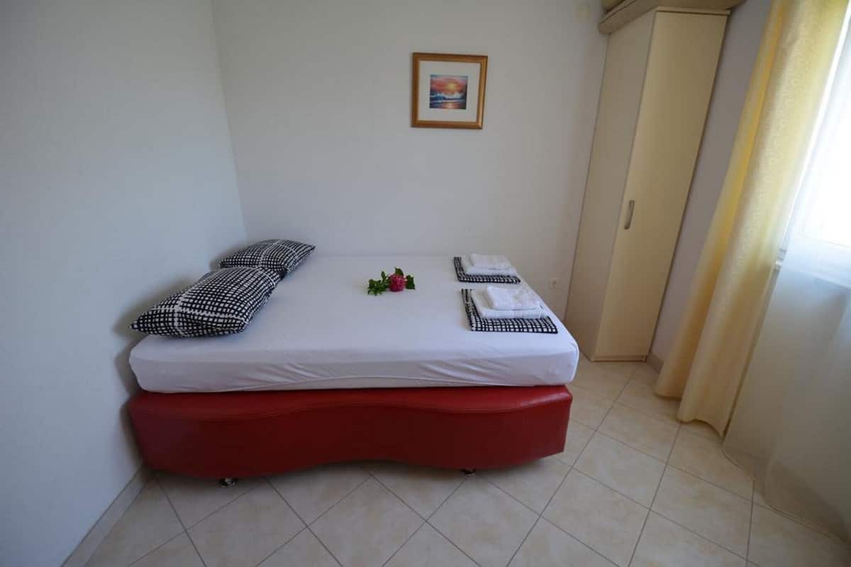 Une petite pièce, bien rangée, avec un lit, un pouf rouge et un tableau encadré accroché au mur.