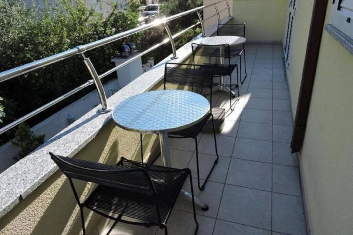 Un balcon avec une table ronde et deux chaises, une rambarde en métal et une vue sur un immeuble et de la verdure.