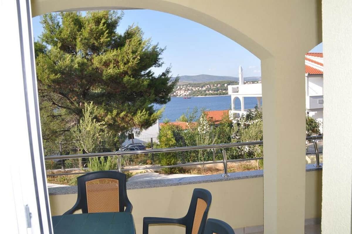 Un balcon avec deux chaises, d’où l’on peut admirer un plan d’eau, des arbres et des bâtiments en arrière-plan.