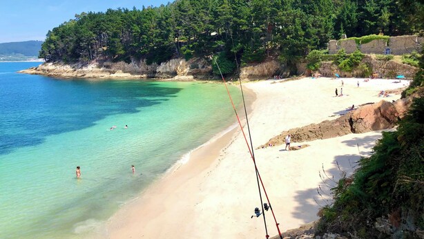 Una playa con agua turquesa cristalina, orilla de arena y un promontorio boscoso.