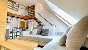 Un espacio habitable moderno estilo loft, con una escalera curva, un comedor y una zona de estar acogedora con un sofá y una mesa de madera.